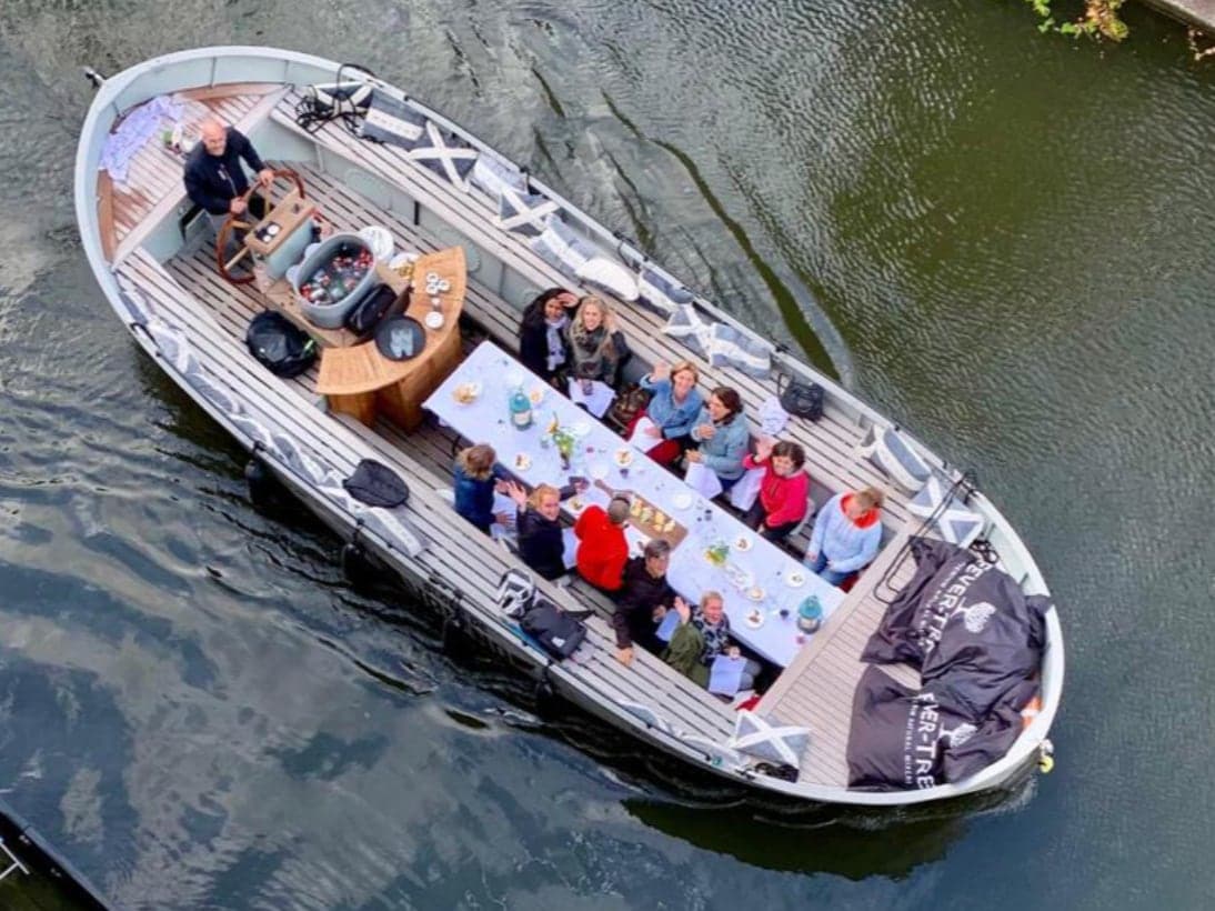 Sloep van bovenaf in de gracht, met een lange gedekte tafel en gasten