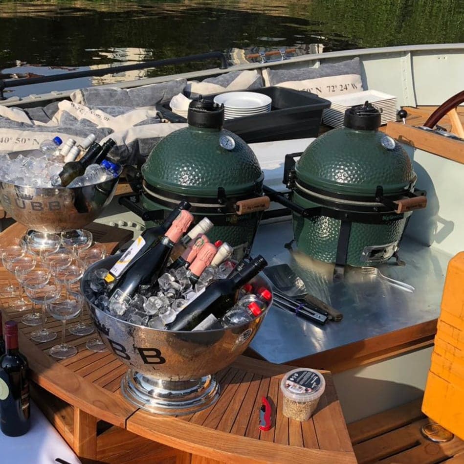 Twee Big Green Eggs en koelers met flessen op de tafel aan boord